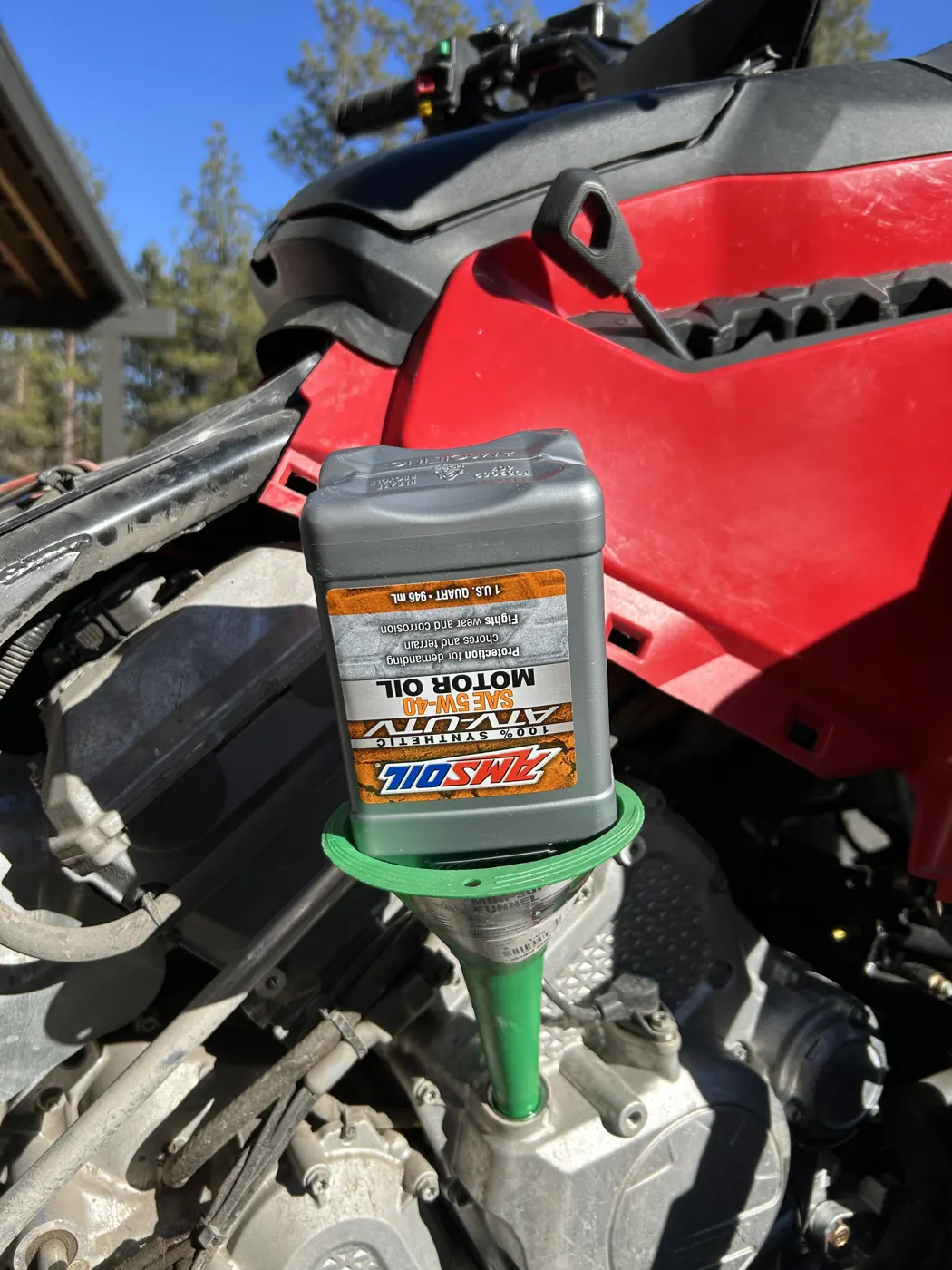 Pouring AMSOIL Synthetic ATV/UTV Motor Oil into an ATV engine through a green funnel