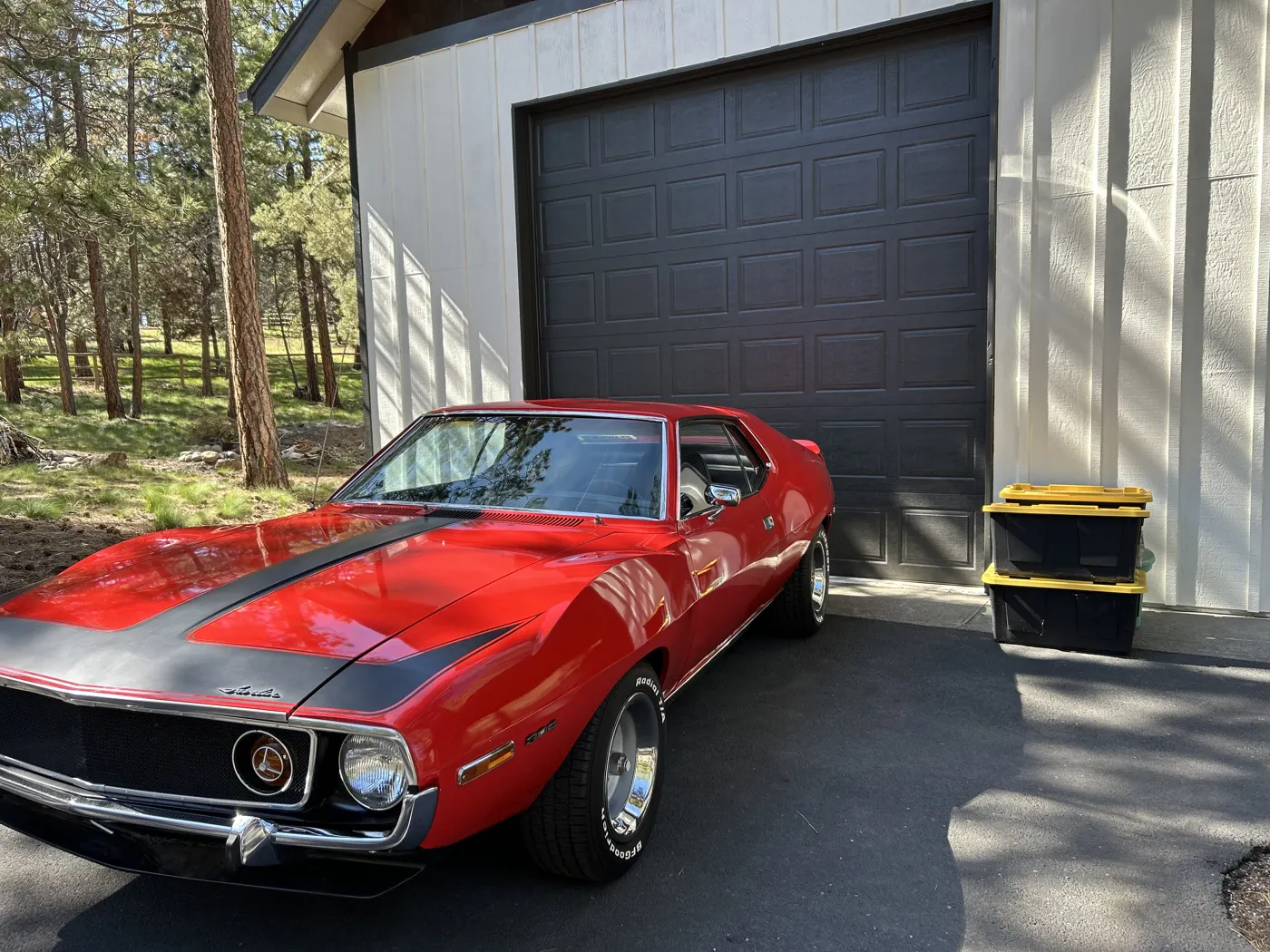 Red classic AMC Javelin muscle car parked in front of a garage